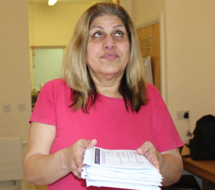 A blind woman wearing a pink T-shirt holds a stack of paper correspondence.
